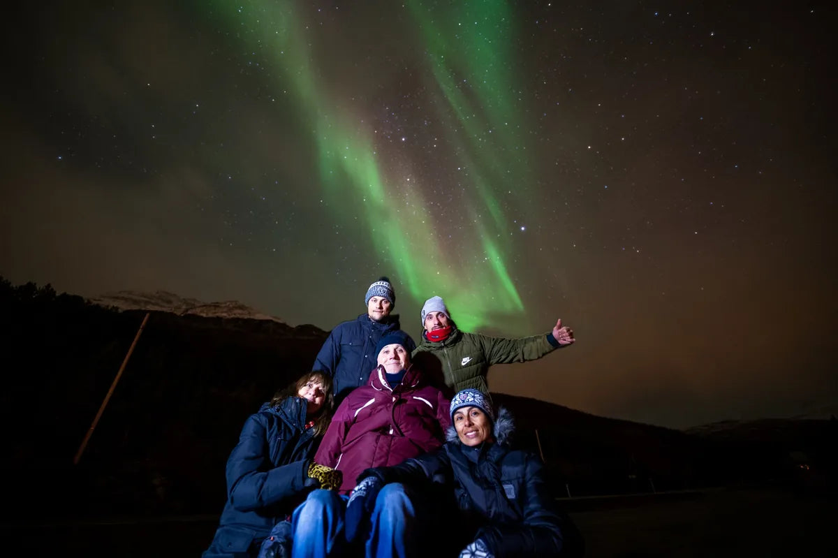 Group of people posing under the Northern Lights in a dark landscape