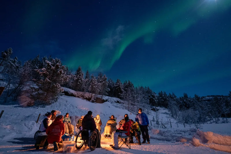 Group of people enjoying the Northern Lights in a snowy landscape